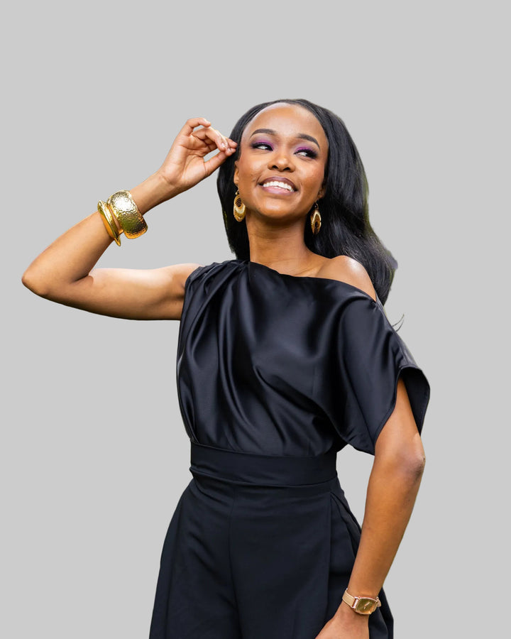 Woman in a black off-shoulder outfit standing outdoors with greenery in the background