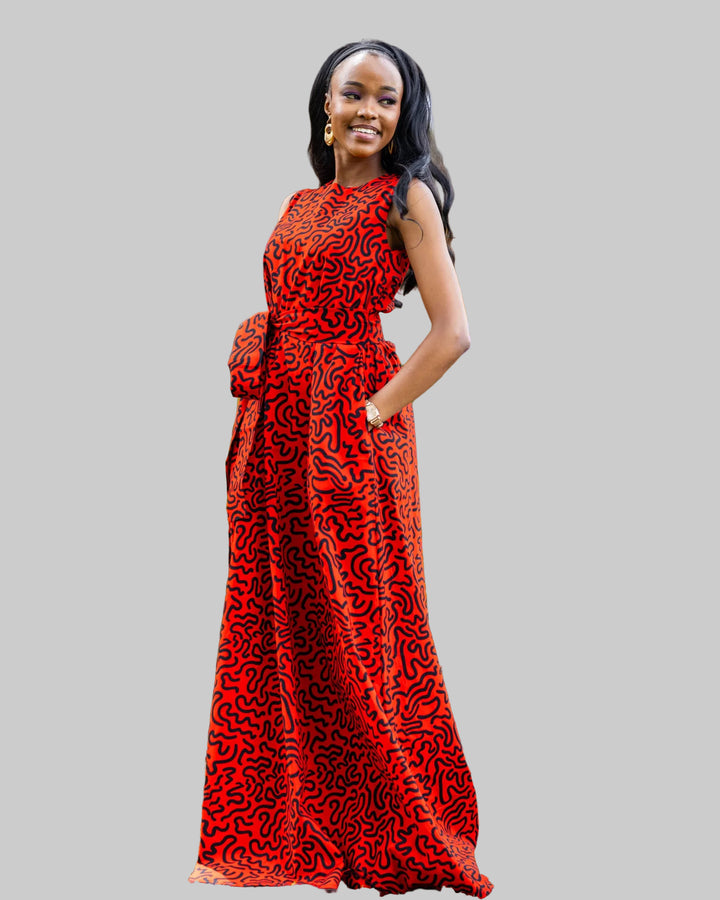 Woman in a red dress standing in a garden with flowers and trees in the background