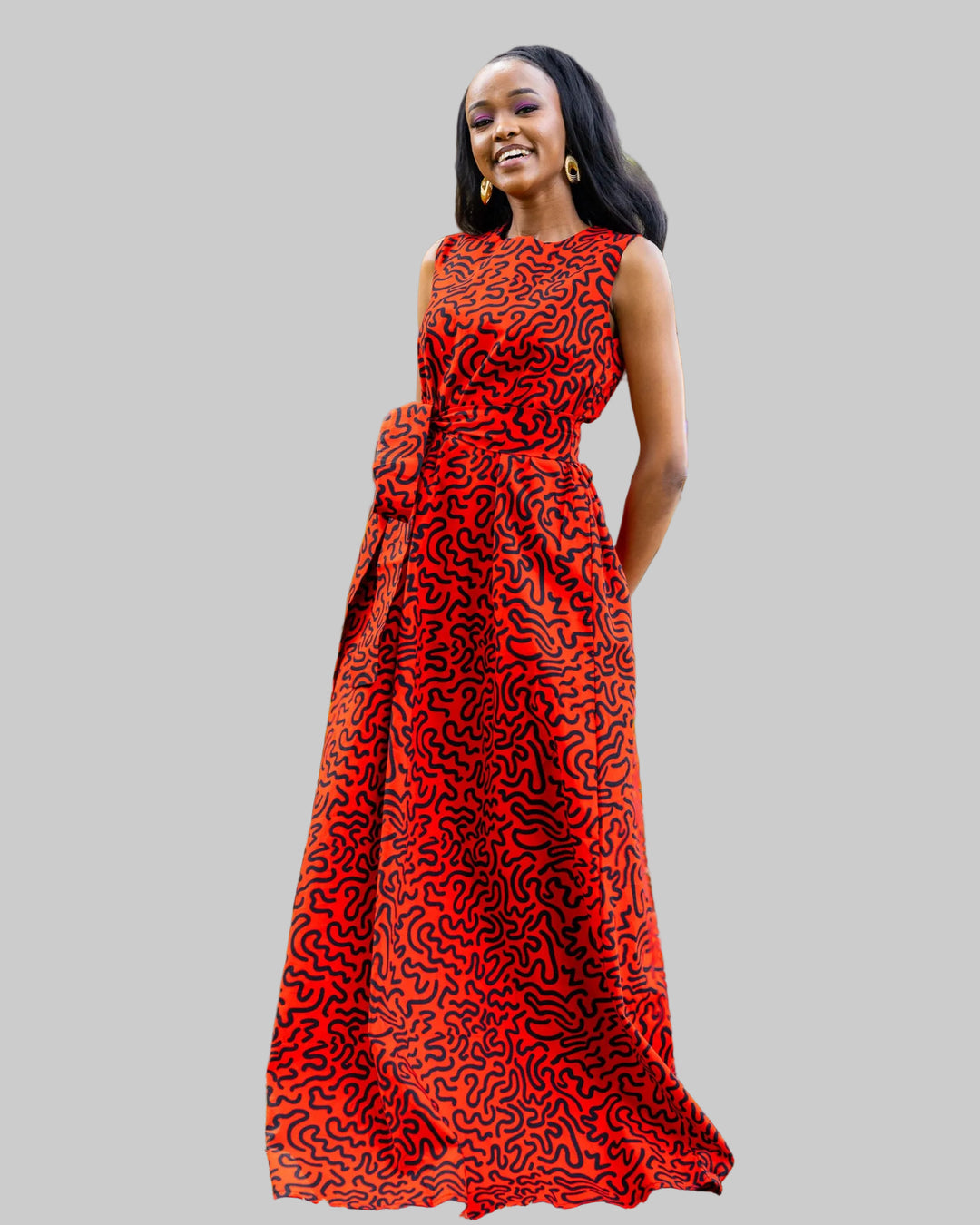 Woman in a red patterned dress standing in a garden with greenery and flowers.